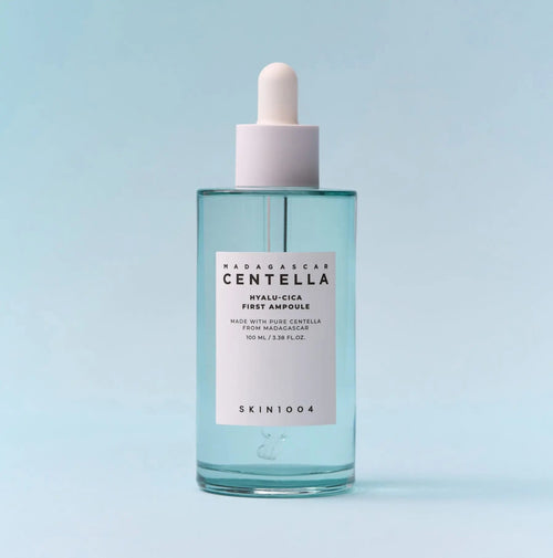 SKIN1004 Madagascar Centella Hyalu-Cica First Ampoule in a clear glass bottle with a white dropper cap, set against a light blue background.