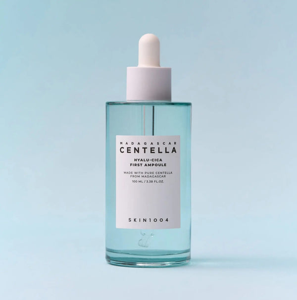 SKIN1004 Madagascar Centella Hyalu-Cica First Ampoule in a clear glass bottle with a white dropper cap, set against a light blue background.